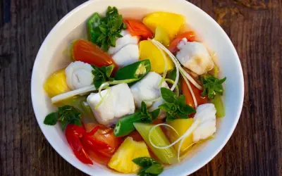 Ein Schüssel Canh Chua mit Fischstücken, Ananas, Tomaten, Okra und Kräutern.