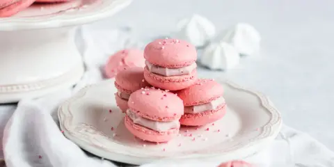 Rosa Macarons mit Himbeer-Ganache-Füllung, bestreut mit Zuckerperlen, auf einem Teller.
