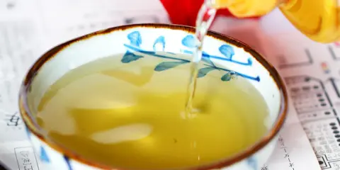 Goldene Flüssigkeit, vermutlich Mirin, wird in eine Schale mit blau-weißen Mustern gegossen.