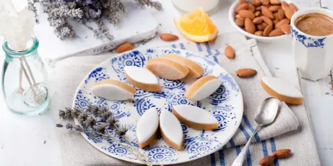 Calissons rezept: Süße Mandelkekse mit weißer Glasur auf blau-weißem Teller, garniert mit Lavendel und Mandeln.