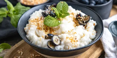 Cremiger Milchreis mit Wasser gekocht, garniert mit Blaubeeren, Minze und gerösteten Kokosflocken. Ein Genuss, der an Kindheit erinnert.