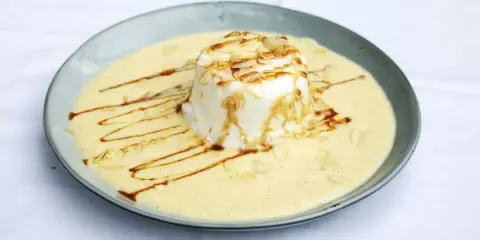 Ein leichtes, schwebendes Dessert aus Eischnee, umgeben von cremiger Vanillesauce, garniert mit Mandelsplittern und Karamell.