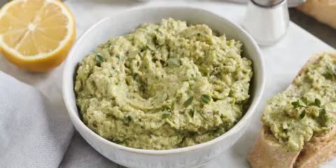 Ein cremiger Zucchini-Aufstrich mit Kräutern und Zitrone, serviert auf Brot.