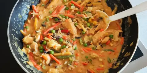 Ein köstliches veganes Curry mit viel Gemüse wie Karotten, Erbsen und Bambussprossen wird in einer Pfanne zubereitet.