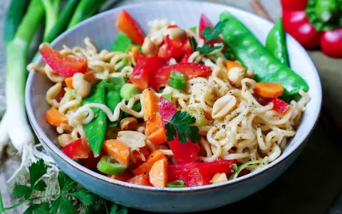 Schüssel mit Nudeln, Erdnüssen, Zuckerschoten, Karotten und Paprika. Ein leckeres Asia Salat Rezept.