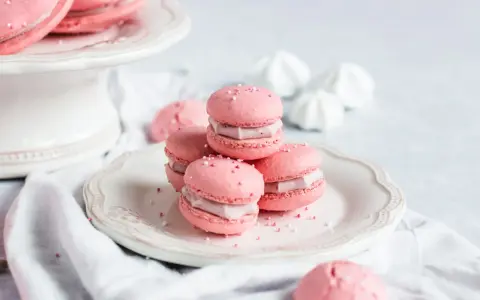 Rosa Macarons mit Himbeer-Ganache-Füllung, bestreut mit Zuckerperlen, auf einem Teller.