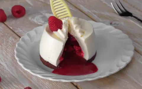 Ausgefallene Desserts zum Vorbereiten: Ein cremiges Dessert mit Himbeersauce und frischer Himbeere, dekoriert mit einem gelben Schokoladen-Detail.