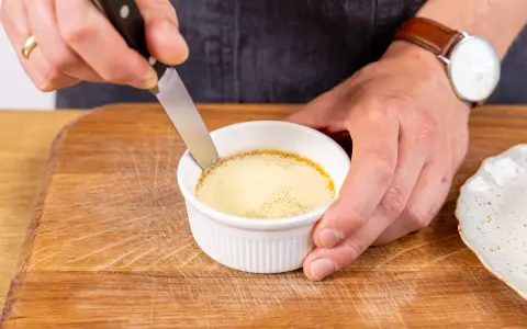 Ein Messer löst den Rand eines cremigen Flan Puddings in einer weißen Keramikschale.