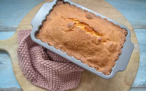 Frisch gebackener, goldbrauner quatre quarts in einer Kastenform, daneben ein rosafarbenes Stricktuch.