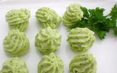 Grüne Kräuterbutter-Tuffs auf weißer Platte, perfekt für Ihre butter rezepte. Frische Petersilie daneben.