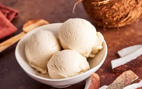 Cremiges Kokoseis selber machen mit Eismaschine: Drei Kugeln in einer Schale, daneben Kokosnussstücke und ein Löffel.
