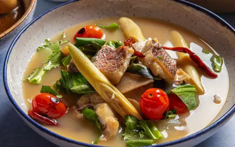 Eine dampfende Schüssel mit **thai Fischsuppe**, garniert mit Kirschtomaten, Kräutern und Zitronengras.