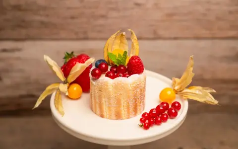 Ein kleiner Charlotte Kuchen, verziert mit frischen Beeren, Physalis und einem Hauch Puderzucker.
