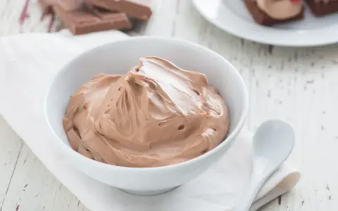 Cremige Schokoladen-Namelaka in einer Schüssel, daneben ein Löffel und Schokoladenstücke.