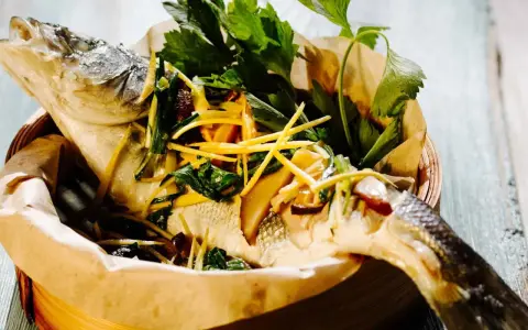 Gedämpfter Fisch, asiatisch zubereitet, mit Ingwer, Frühlingszwiebeln und frischen Kräutern in einem Bambuskorb.