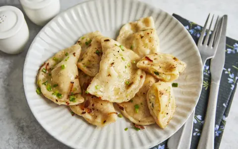 Hausgemachte Tworog Rezepte: goldbraune Teigtaschen, gefüllt mit Quark, bestreut mit Schnittlauch und Röstzwiebeln.