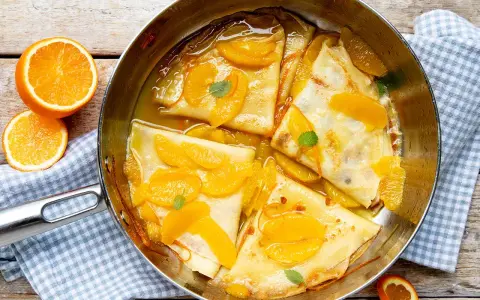 Crêpes Suzette im Originalrezept: zarte Pfannkuchen in Orangensauce mit frischen Orangenspalten und Minze garniert.