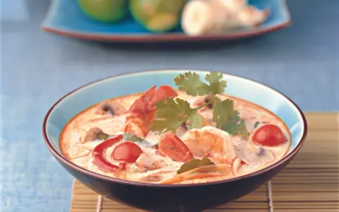Eine cremige garnelensuppe asiatisch mit Garnelen, Pilzen und Tomaten, garniert mit Koriander.