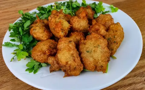 Knusprige Accras de Morue, goldbraun frittiert und mit frischer Petersilie garniert, auf einem weißen Teller.