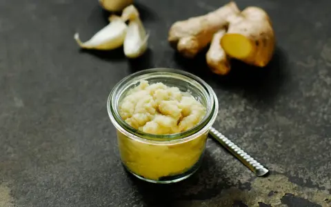 Frisch zubereitete ingwer knoblauch paste in einem Glas, daneben Ingwerwurzel und Knoblauchzehen auf dunklem Untergrund.