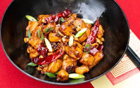 Ein köstliches Gericht mit asiatischen Rezepten mit Huhn, garniert mit Chilis und Frühlingszwiebeln in einer schwarzen Schüssel.