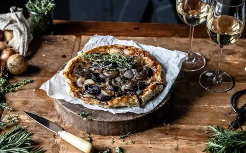 Herzhafte Tarte Tatin mit karamellisierten Zwiebeln und frischen Kräutern, serviert mit Weißwein.
