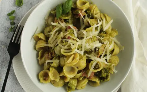 Orecchiette-Pasta mit grünem Pesto, Speck und geriebenem Parmesan. Ein köstliches Gericht, das zeigt, wie vielseitig Rezepte mit Pistazienmus sein können.