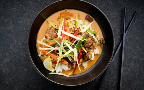 Ein aromatischer Thai Curry Rind mit Reis, Karotten und frischen Kräutern, garniert mit Limette.