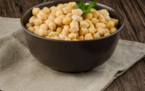 Schüssel mit Kichererbsen, die auf einem Leinentuch auf Holzhintergrund steht. Keine Sorge, Kichererbsen aus der Dose sind nicht giftig!