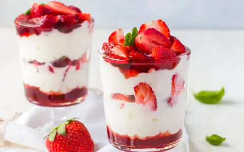 Zwei Gläser mit Erdbeer Mascarpone Creme, geschichtet mit frischen Erdbeeren und Erdbeersauce, garniert mit Minze.