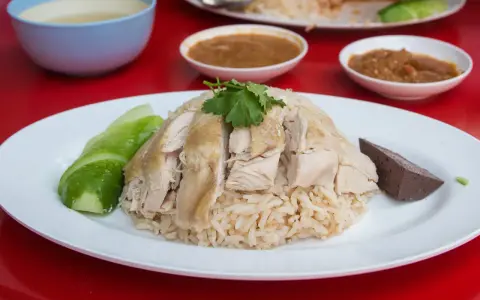 Khao Man Gai: gedämpfter Reis mit zartem Hühnchen, Gurkenscheiben und einer Blutwurstscheibe, garniert mit Koriander.
