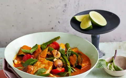 Ein köstliches Panang Curry mit Fisch, Kürbis, grünen Bohnen und Tomaten, garniert mit frischem Basilikum und Limettenspalten.