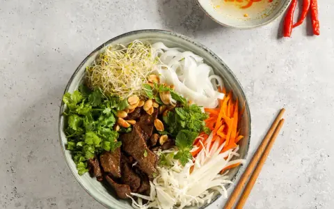 Bun bo nam bo: Reisnudeln, Rindfleisch, Sprossen, Karotten, Kohl und Kräuter in einer Schüssel, garniert mit Erdnüssen.