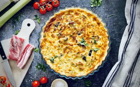 Herzhafte Quiche mit Speck und Lauch, perfekt für herzhafte Quiche Rezepte. Dazu frische Tomaten und Kräuter.