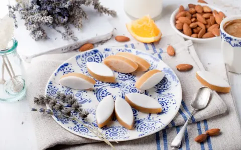 Calissons rezept: Süße Mandelkekse mit weißer Glasur auf blau-weißem Teller, garniert mit Lavendel und Mandeln.