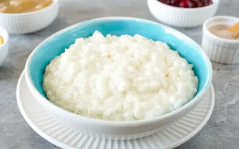 Cremiger Milchreis in einer blauen Schüssel, daneben Schüsseln mit Apfelmus, Kirschen und Zimt. Ein köstlicher Reis-Genuss.