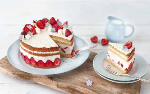 Eine köstliche Erdbeer Basilikum Torte mit frischen Erdbeeren und Sahne, ein Stück davon auf einem Teller.