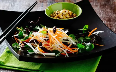 Ein bunter Papaya Salat vietnamesisch mit Karottenstreifen, Kräutern und gerösteten Erdnüssen.