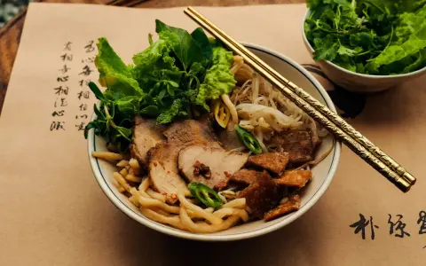 Cao Lau: Nudelschüssel mit Schweinefleisch, Sprossen und Kräutern, garniert mit knusprigen Krusten. Goldene Stäbchen ruhen auf dem Gericht.