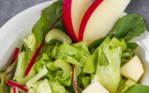 Frischer Romana Salat mit Apfelstücken und roten Mangoldblättern in einer weißen Schüssel.