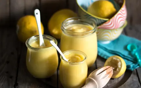 Leichte Zitronencreme im Thermomix zubereitet, serviert in Gläsern mit Löffeln, daneben frische Zitronen und ein Zitruspresse.