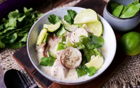 Ein cremiger Thai Green Curry mit Hühnchen, Zucchini, Zuckerschoten und Auberginenscheiben, garniert mit Limettenspalten und Koriander.
