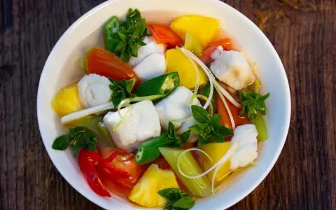 Ein Schüssel Canh Chua mit Fischstücken, Ananas, Tomaten, Okra und Kräutern.