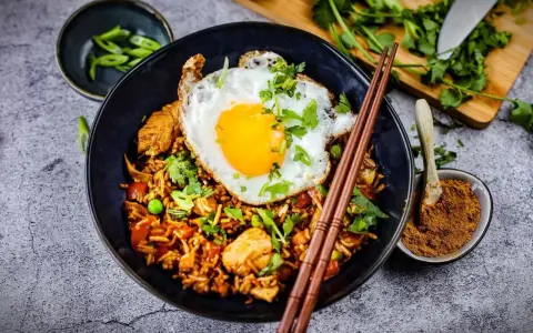 Was ist Nasi Goreng? Ein Teller mit gebratenem Reis, Hühnchen, Erbsen und einem Spiegelei, garniert mit Koriander und Frühlingszwiebeln.