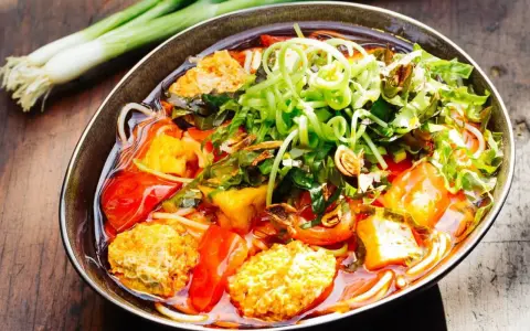 Herzhaftes Bun Rieu mit Tofu, Tomaten und frischen Kräutern, garniert mit Frühlingszwiebeln.