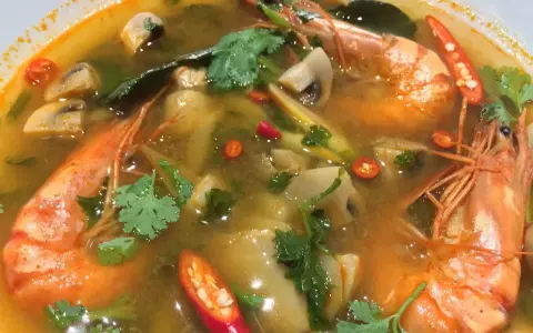 Eine dampfende Schüssel mit scharfer Thai Suppe, gefüllt mit Garnelen, Pilzen und Chili.