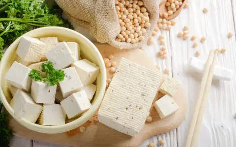 Frischer Tofu, ein toller Fleischersatz, liegt neben Sojabohnen und Petersilie.
