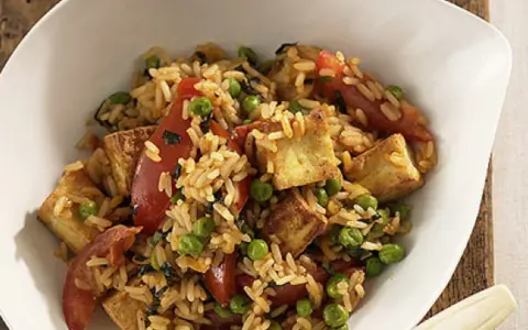 Herzhafter pilaw reis mit gebratenem Tofu, Erbsen und Tomatenstücken in einer weißen Schüssel.