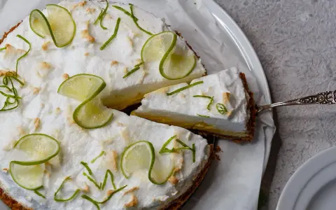 Eine köstliche Limetten Tarte mit luftiger Baiserhaube, garniert mit frischen Limettenscheiben und Zesten. Ein Stück wird gerade serviert.