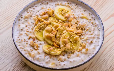 Schüssel mit cremigem vietnamesischem Dessert, garniert mit Bananenscheiben, Erdnüssen und Sesam.
